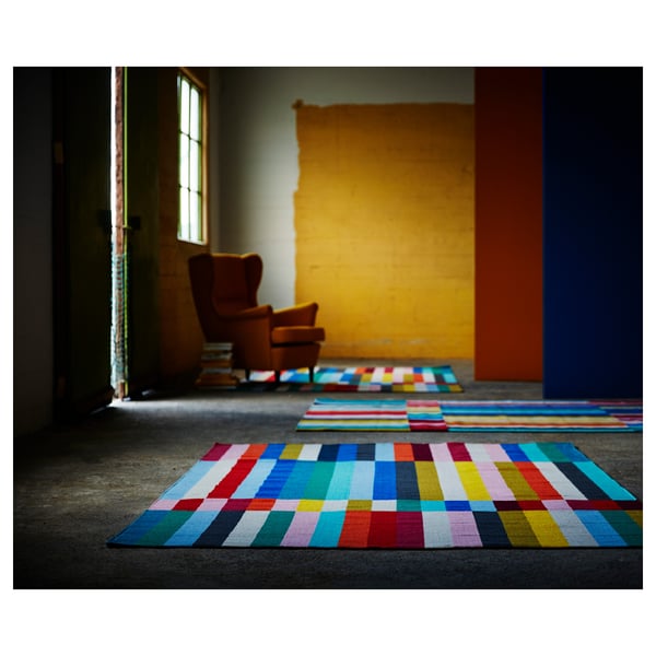 Vibrant multi-colored striped rugs, handwoven from wool. Bright colours on dark floor, displayed indoors.