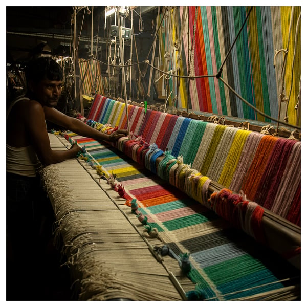 Person operating colourful loom, weaving vibrant, multicoloured fabric.