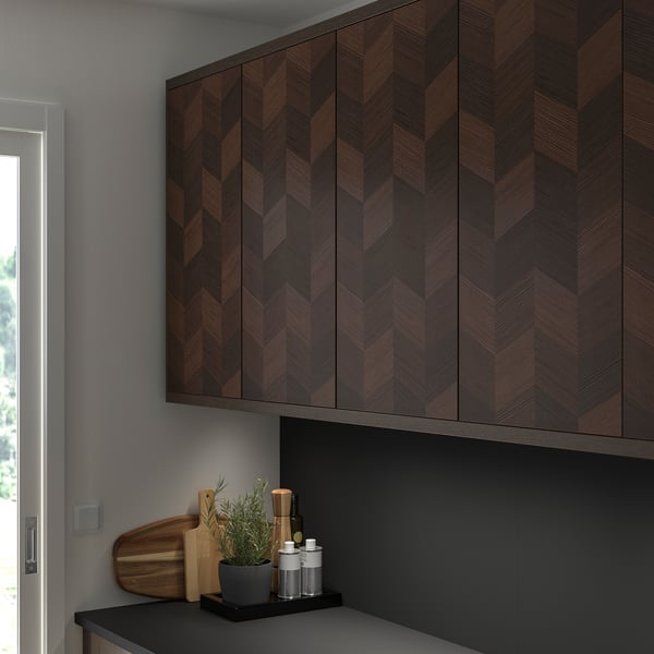 Brown herringbone wooden cabinets with cutting board, plant, and items on countertop.