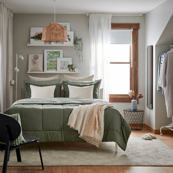 Bedroom with HEDFRYLE green comforter, pillows, and decor; wooden furniture; large window.