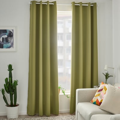 Green HILLEBORG curtains cover large window. Made from recycled polyester, they block light effectively. Room white walls, couch, and cactus.