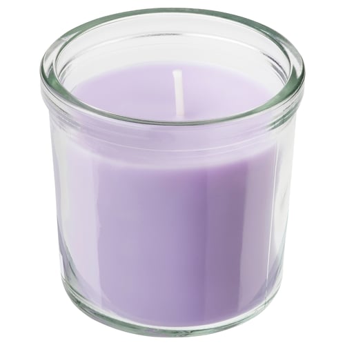A lavender-colored scented candle in a clear glass jar. The cylindrical shape allows for a calm and welcoming ambiance, ideal for home decor.