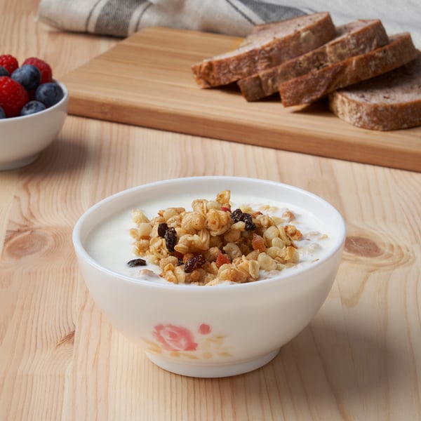 Bowl of cereal on wooden table, accompanied by berries and bread.