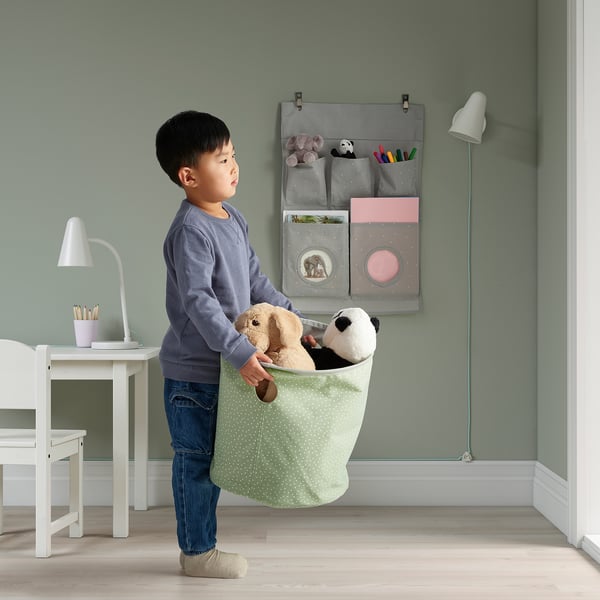 Young boy holding reversible toy bag, which stands upright and organises stuffed animals, with pastel polka dots pattern visible.