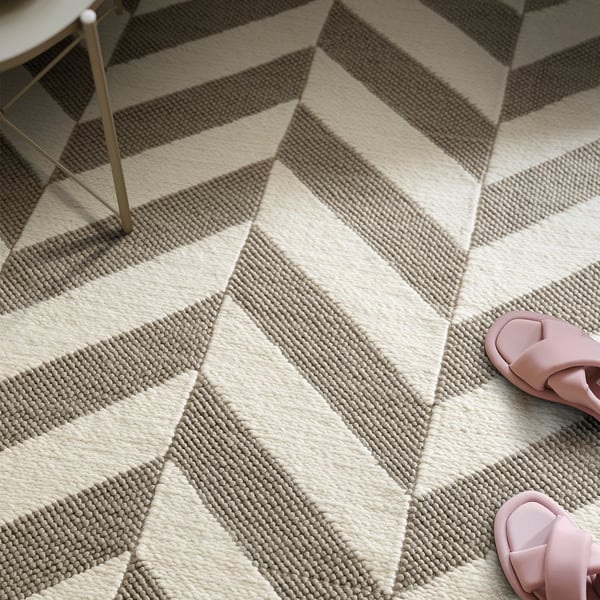 Striped wool rug with beige and grey stripes. Pink sandals on top, metal chair leg seen.
