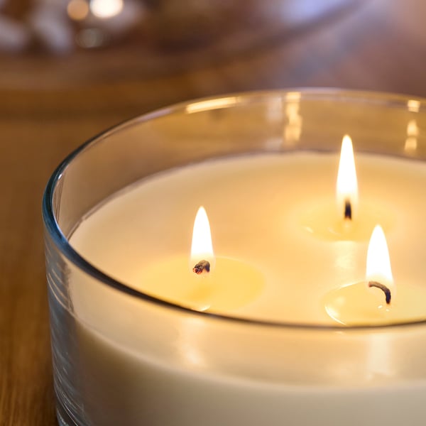 Scented candle with three lit wicks in clear glass container, emitting warm, inviting glow.