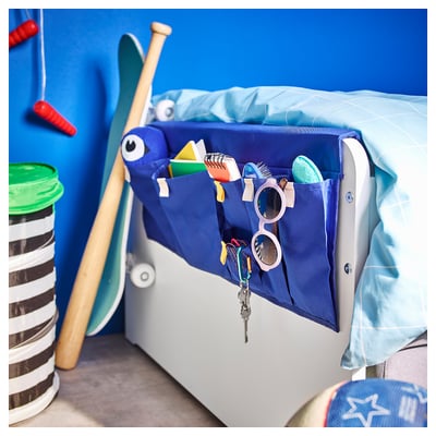 Blue childrens bed pocket with monster design holds various items. Made of polyester. Attaches to bed frame.