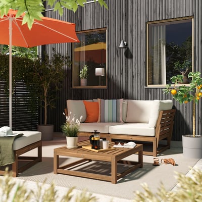 Cosy outdoor patio with NÄMMARÖ beige cushioned sofa, wooden coffee table, orange umbrella, plants, and potted tree.