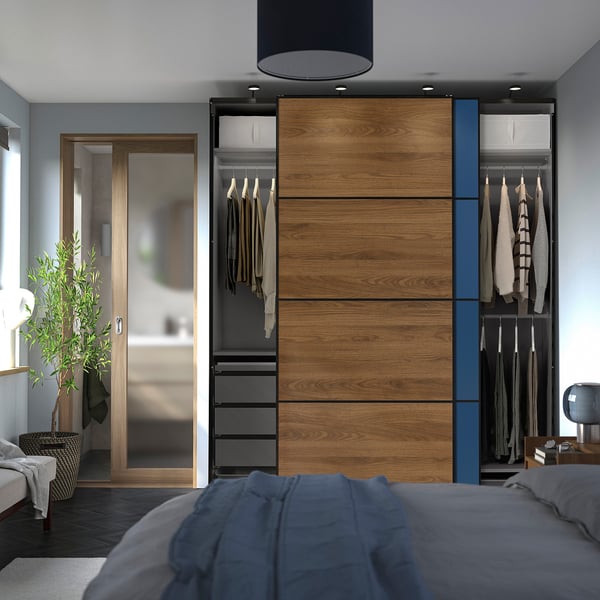 Bedroom with modern PAX wardrobe. Sliding doors, hanging clothes, drawers. Grey bedding, plant, mirror, and lamp visible.
