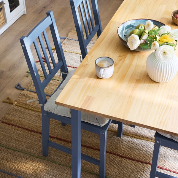 Wooden dining table with blue chairs, cup, flowers, vase, on jute rug, cosy, compact.
