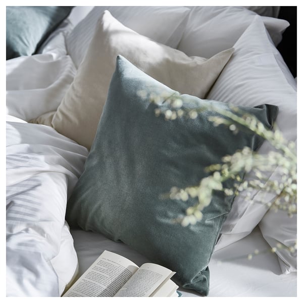Cosy bed with green SANELA velvet pillow, white linens, and open book. Soft, inviting decor.