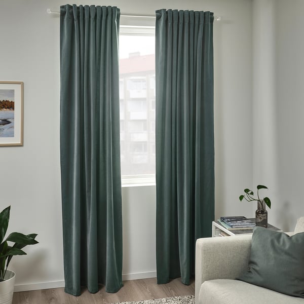 Grey-green velvet SANELA curtains frame window, floor-length. Elegant, private, flanked by white couch and plants.