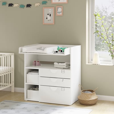 Small white baby changing station with shelves, drawers, and toys on top.