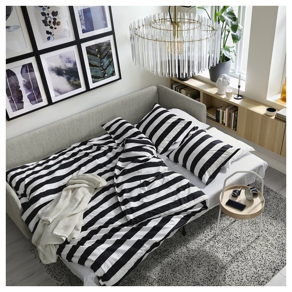 Modern living room with SÖDERHAMN sofa-bed, striped black & white bedding, coastal decor, and plant.