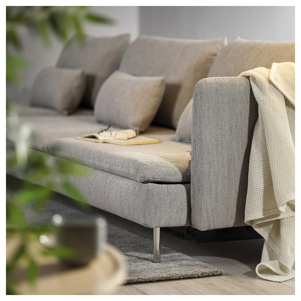 Modern grey sofa bed with cushions and blanket. Light wood floor and plant.