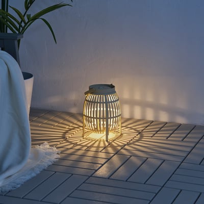 Small SOLVINDEN lantern on deck, lit, surrounded by shadows, near plant & blanket.