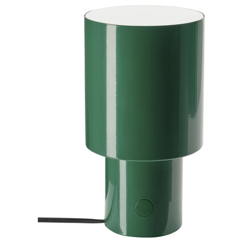A green SPETSBOJ table lamp. It is cylindrical with a glossy finish and a round button on the side for control. The sleek design adds a modern touch.