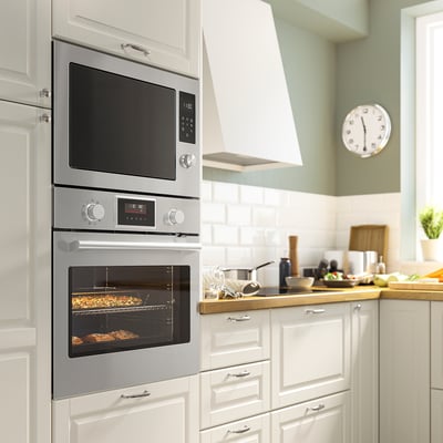 Stainless steel built-in microwave and oven combo in a modern white kitchen, with a clock and cooking utensils on the counter.