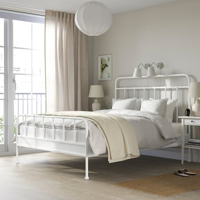 Modern white bed near window with neutral linens, stylish lamp, side table decor, cosy room.