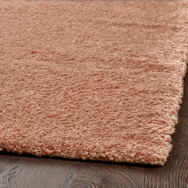 Soft, peach-colored rug with dense, low pile, laid on dark wood floor. Quality texture feels comfortable and cosy.