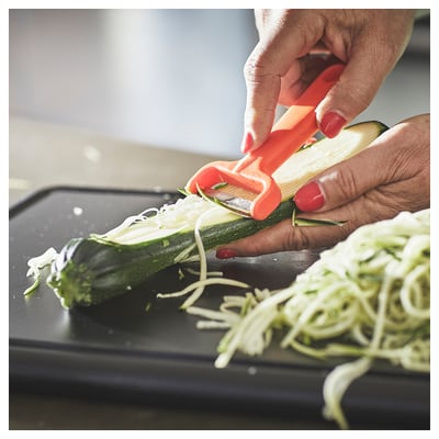 Person slicing cucumber with orange UPPFYLLD cutter on black board.