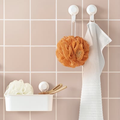 Simple bathroom storage: white basket, orange body puff, hanging towel on pink wall tiles.