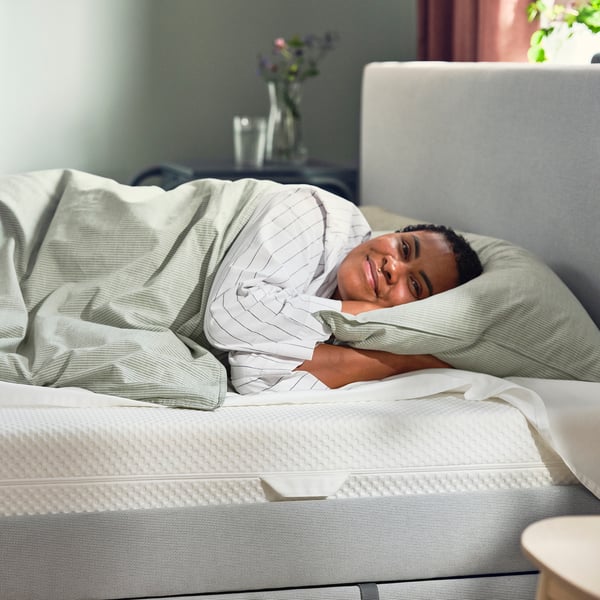 Person sleeping comfortably on white ÅBYGDA mattress, striped green bedding.