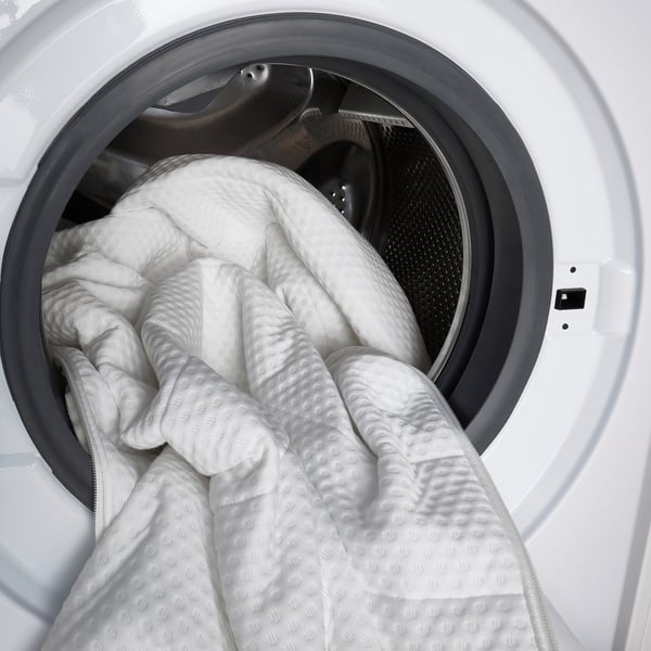 Image shows a white hamper, partially filled with crumpled white laundry items. The hamper is open, revealing the contents inside.
