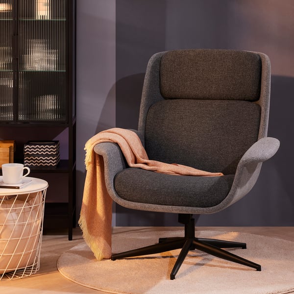 Cosy ÄLEBY grey armchair with black base, draped blanket, on round rug near white side table with cup.