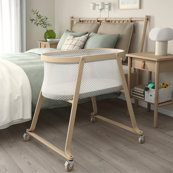 Modern nursery with white ÄLSKVÄRD bassinet near bed. Mesh sides, wooden frame, casters for easy movement.