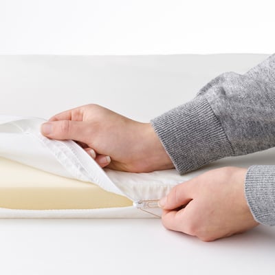 Person placing a white mattress into a bassinet.