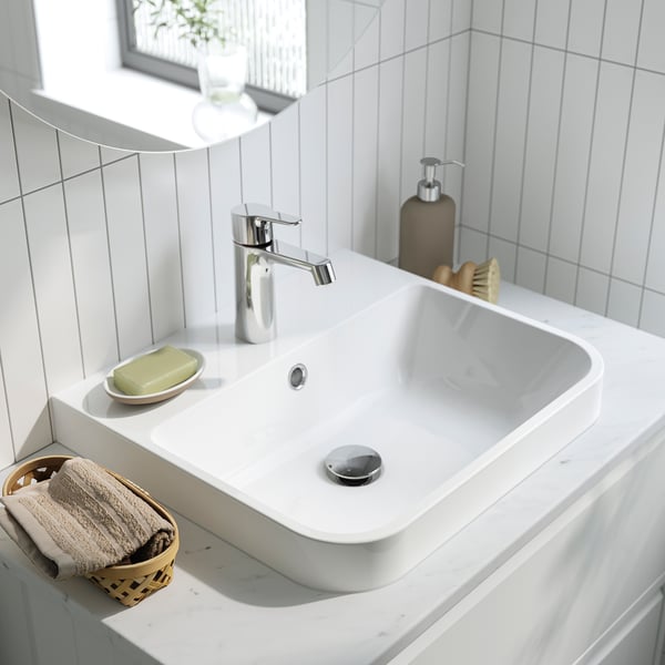 Modern white bathroom sink with chrome tap, soap dish, soap dispenser, and towel basket with towels.