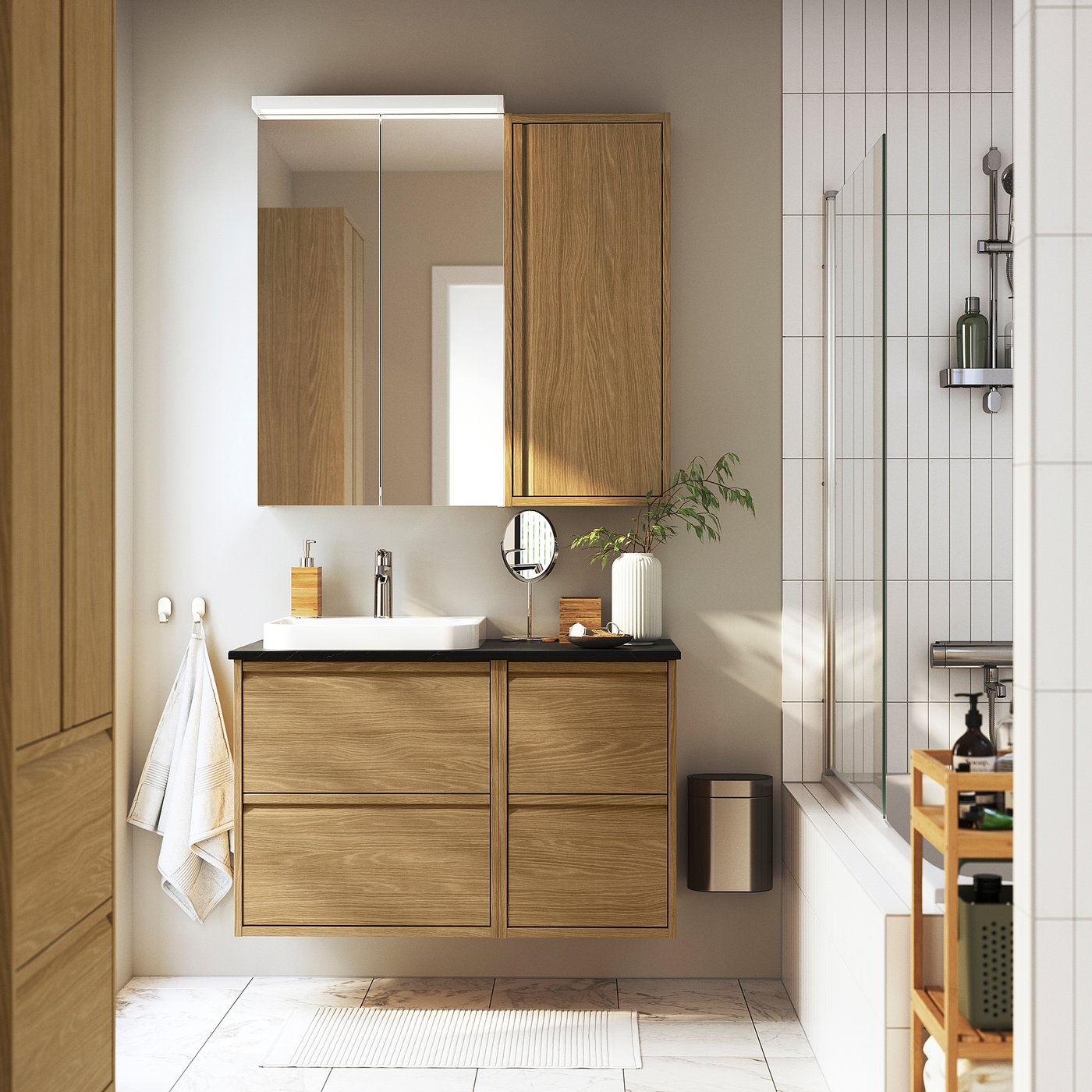 Modern bathroom with ÄNGSJÖN collection: floating light brown vanity, mirror, vessel sink, glass shower, wooden rack.
