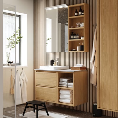 Modern bathroom with light wood ÄNGSJÖN vanity, white marble sink, large mirror, open shelves, and hanging towels.