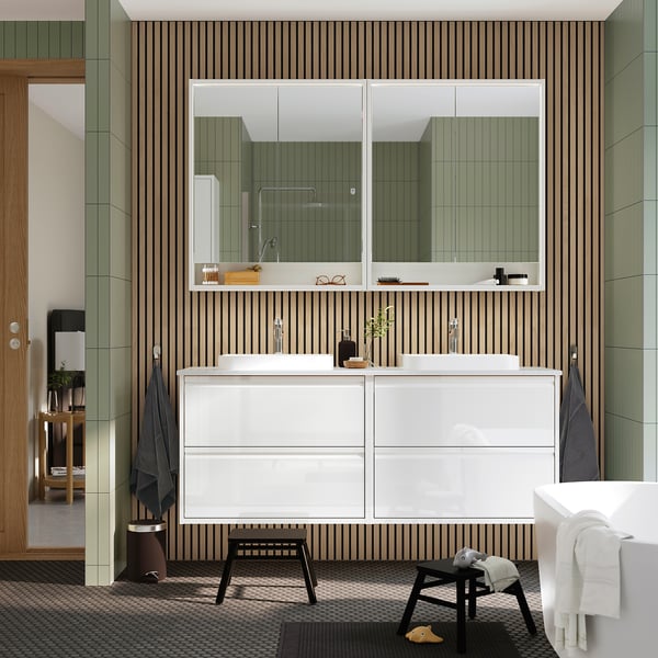 Modern white vanity with two sinks, cabinets, mirror, and green wall. Towels and bathtub.