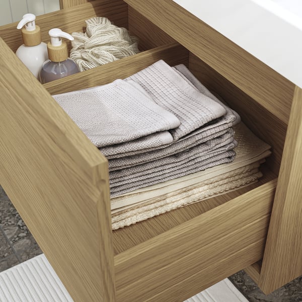Wooden bathroom drawer open, revealing neatly folded towels and bottles, showcasing storage functionality.