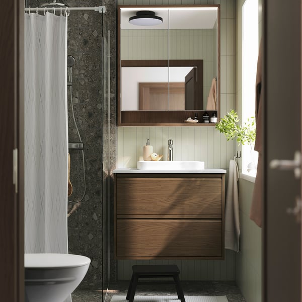 Modern bathroom with brown oak vanity, marble basin, large mirror, and shower curtain. Black stool in front.