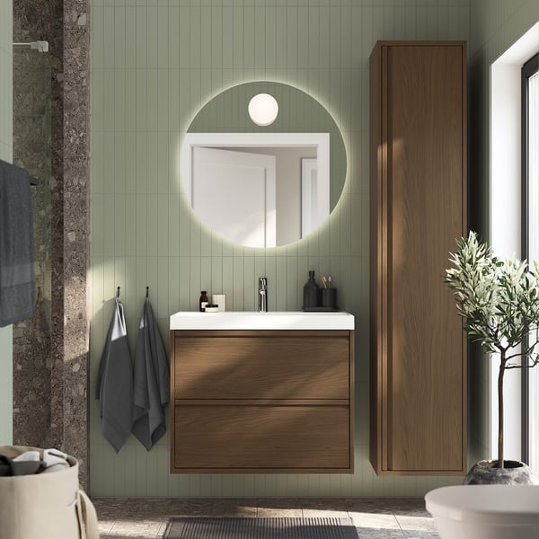 Wall-mounted light brown vanity, square sink, round mirror, wooden cabinet, grey towels, olive tree.