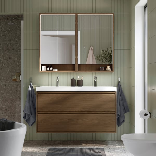 Modern bathroom with large wooden cabinet, double sink, mirrored medicine cabinet, hanging blue towels, and grey tiled floor.