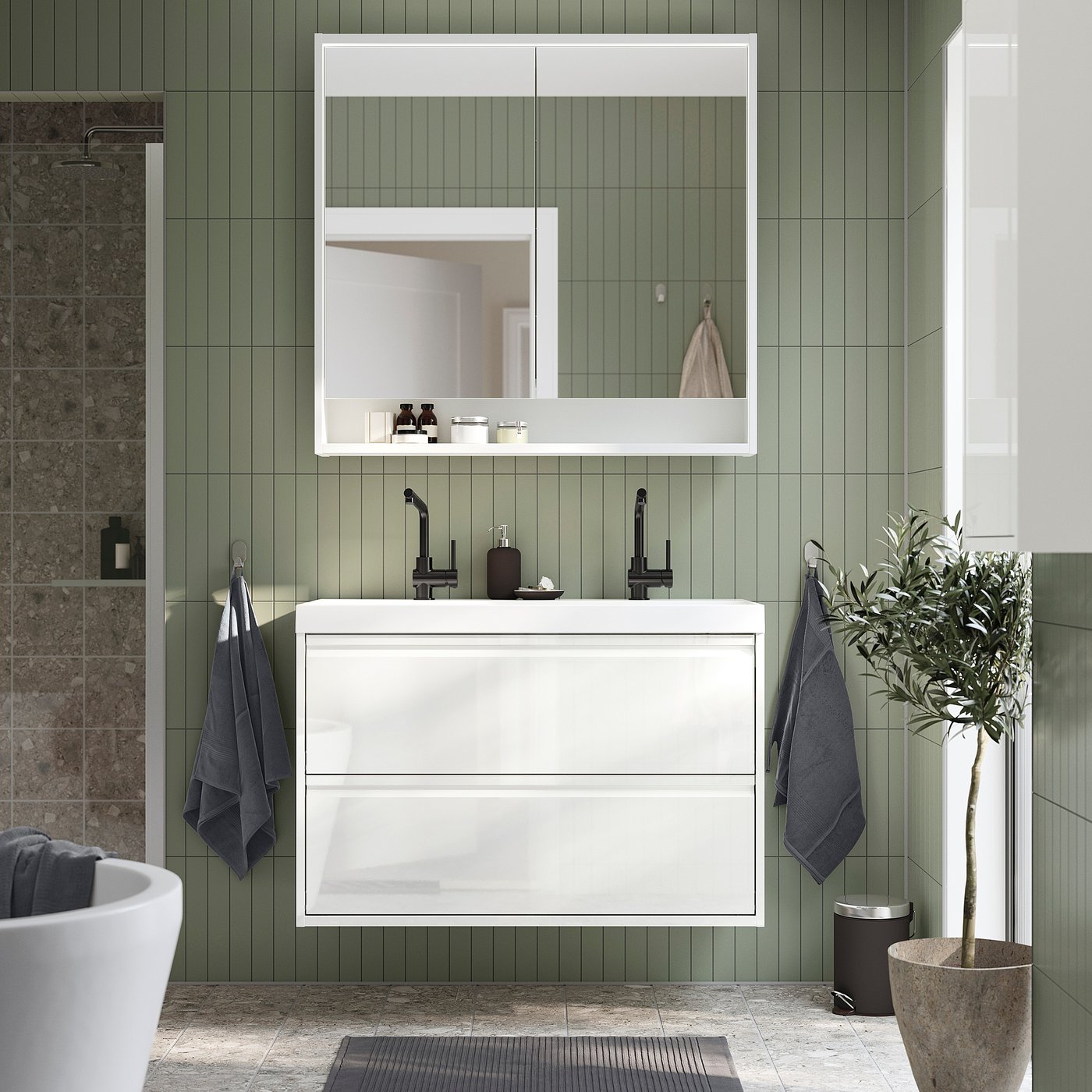 Modern white ÄNGSJÖN vanity with 2 drawers, black fixtures, green walls, mirror with lights, plant, grey towels.