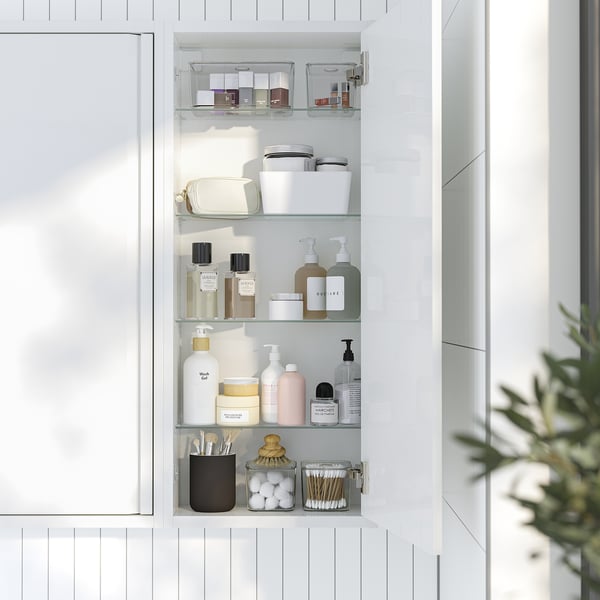 Open white wall cabinet with glass shelves, displaying toiletries like bottles, jars, and make-up tools.