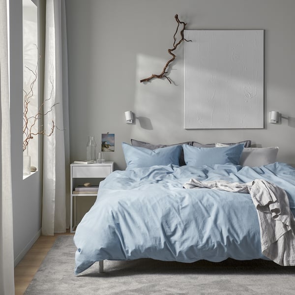 Grey ÄNGSLILJA bedding on low bed, white artwork, simple bedside table.
