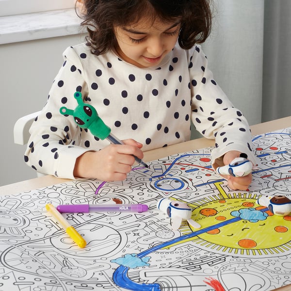 A young girl uses finger puppets to colour a space-themed placemat, engaging in creative play.