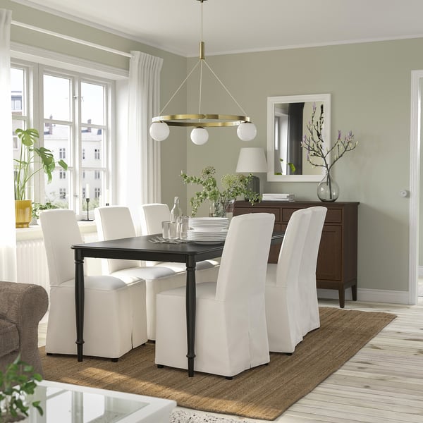 Modern dining room with brass pendant lamp, glass globes, white chairs, green wall, plants, wood floor.