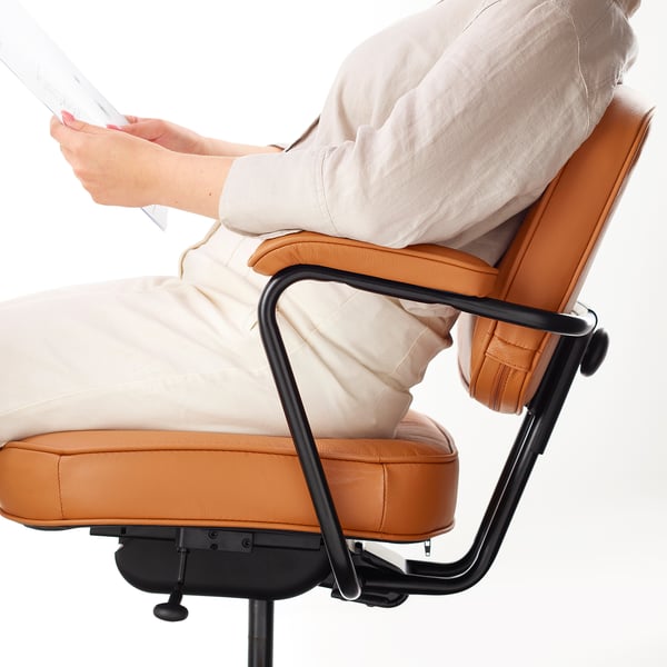 Person sitting in ergonomic office chair with adjustable lumbar support and padded armrests.