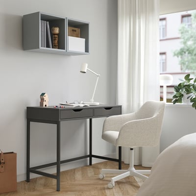 Modern home office with ALEX black desk, adjustable lamp, grey chair, and wall shelf. Large window with curtains lets in natural light.