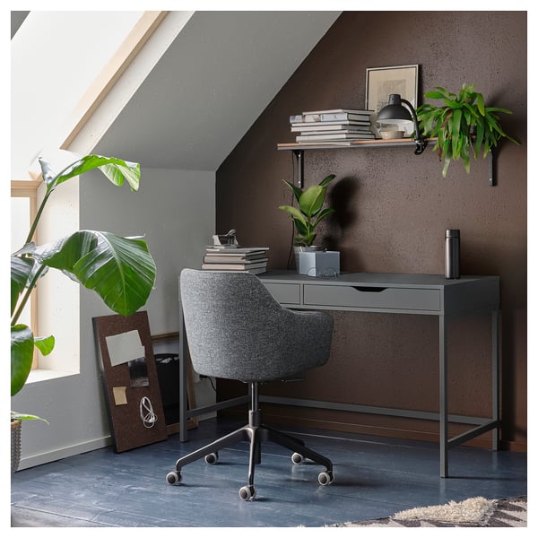 Modern grey desk with drawers, a black chair, green plants, and a shelf with books.