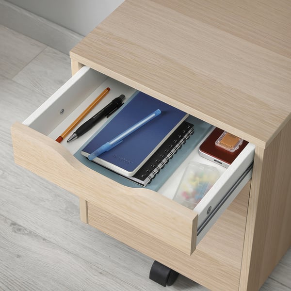 Open wooden drawer with organised office supplies: pens, pencils, notebooks, and a ruler.