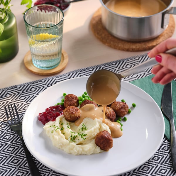 A meal featuring meatballs, mashed potatoes, and peas on a white plate with gravy being poured from a ladle.