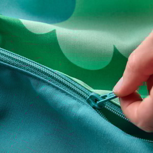 Person zipping up green, tree-patterned baby support cushion.